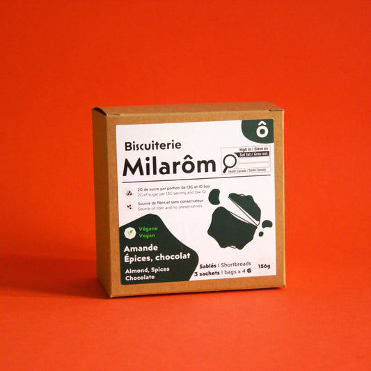 Cette image montre sur un fonds rouge notre boîte de 12 biscuits sablés à l'amande, épices et chocolat ; nous utilisons dans nos recettes un mélange d'épices sur une base de cannelle qui donne un goût réconfortant à nos biscuits sablés ; nous n'utilisons pas de beurre et d'oeufs et les remplaçons par l'huile de coco désodorisée pour une version végane