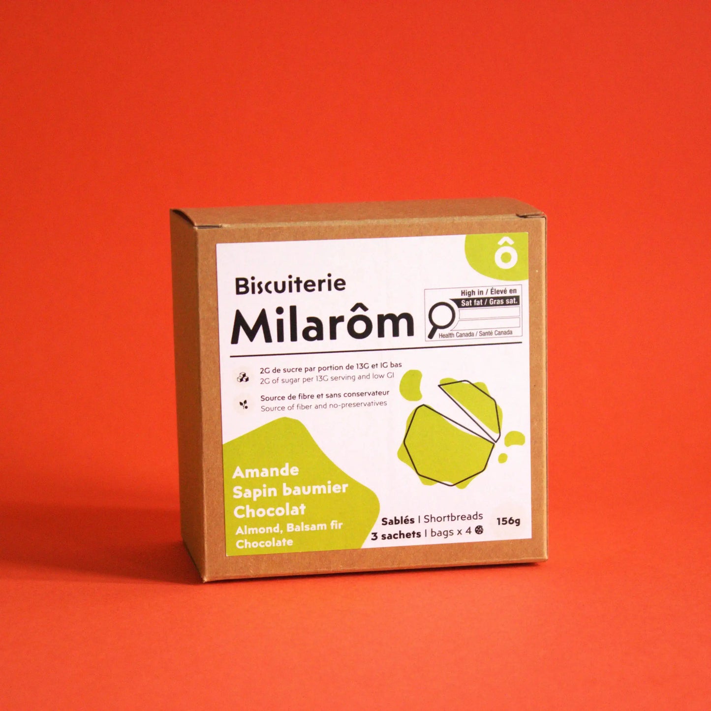Cette image montre sur un fonds rouge notre boîte de 12 biscuits sablés à l'amande, sapin baumier et chocolat ; nous utilisons dans nos recettes des des amandes torréfiées et de la poudre de de jeunes pousses de sapin baumier de Gaspésie
